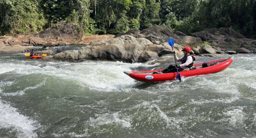 A person wearing safety gear paddles a red kayak through whitewater.